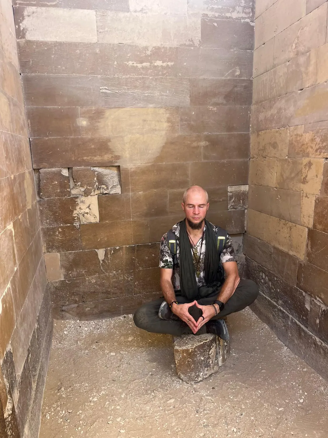 Tyler seated cross-legged in meditation on a stone block inside a bare stone chamber