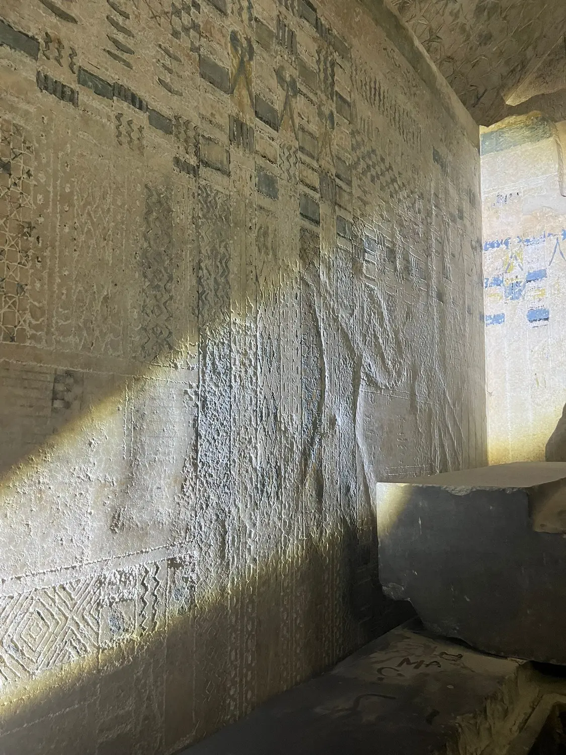 A diagonal beam of sunlight across a wall carved with hieroglyphs inside a stone chamber