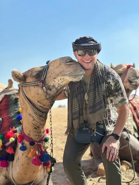 Tyler beside a decorated camel in the desert